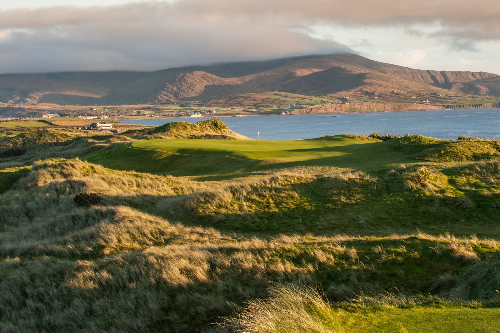 Links fairways winding through grassy dunes beside a bay, with mountains beyond, on the west coast of Ireland